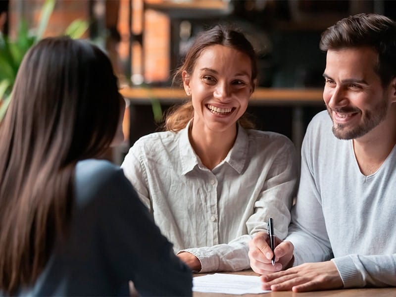 Três pessoas sorrindo e discutindo um documento em um ambiente de trabalho colaborativo. A imagem representa a importância das parcerias estratégicas e colaborações no empreendedorismo, mostrando como trabalhar em equipe pode abrir portas para novas oportunidades e recursos.