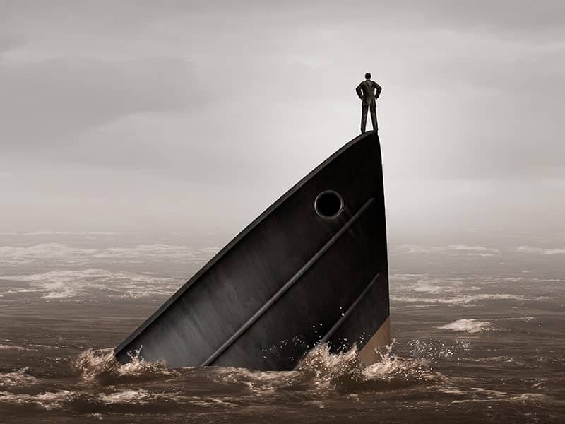 Homem de pé na proa de um navio afundando em um mar tempestuoso. A imagem simboliza o desafio de enfrentar adversidades e o risco de fracasso no empreendedorismo, destacando a importância de resiliência e estratégia para superar momentos difíceis.