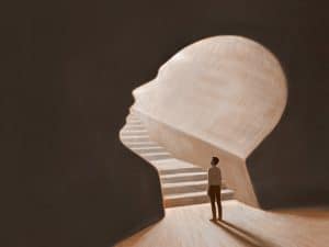 Ilustração de uma pessoa de pé na base de uma escada que leva ao interior de uma cabeça humana esculpida, simbolizando o conceito de mente empreendedora. A imagem representa a jornada de desenvolvimento pessoal e profissional necessária para alcançar o sucesso no empreendedorismo.